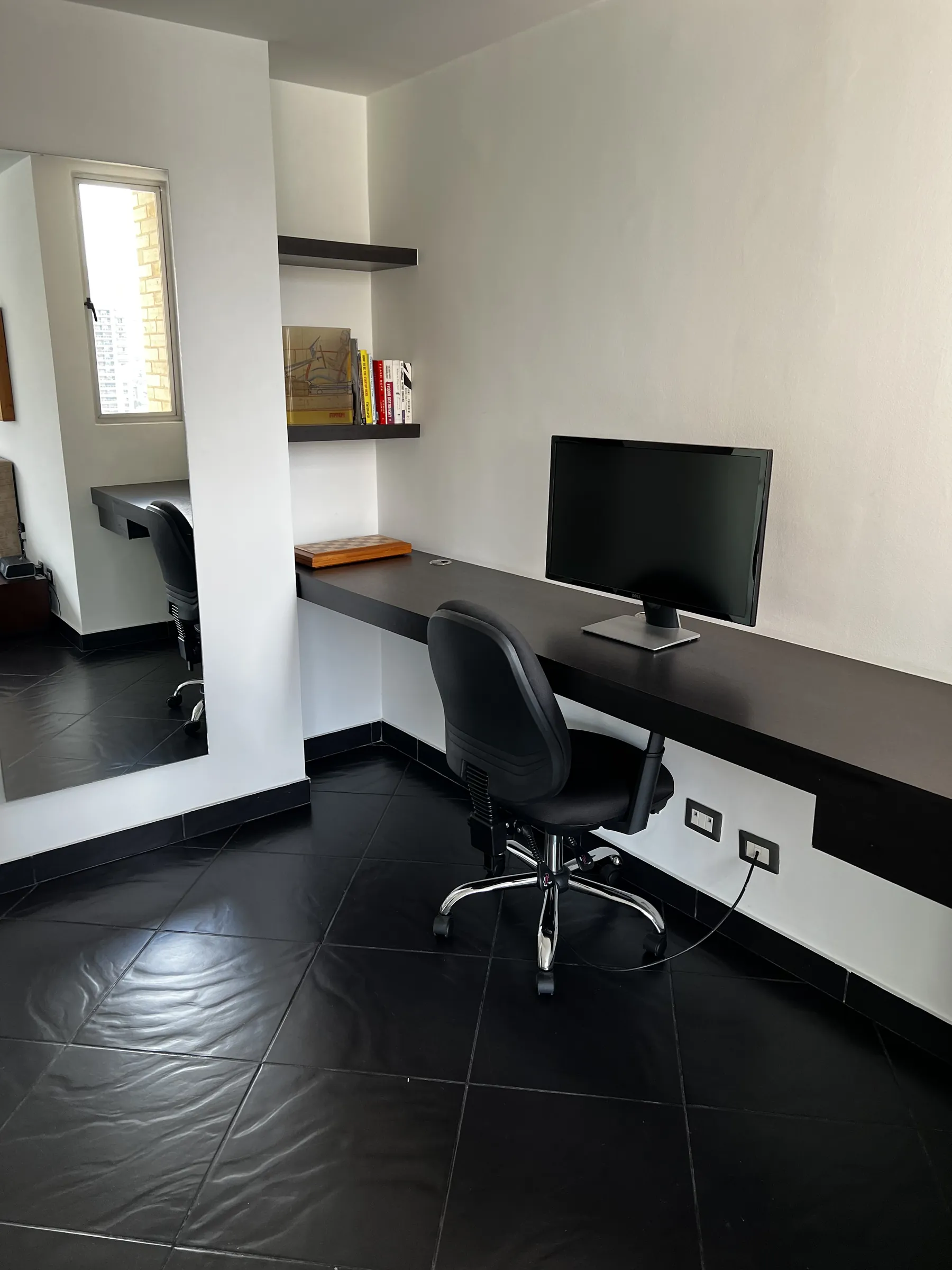 Built-in dark timber desk and floating shelves beside a tall window, with a second work station beyond
