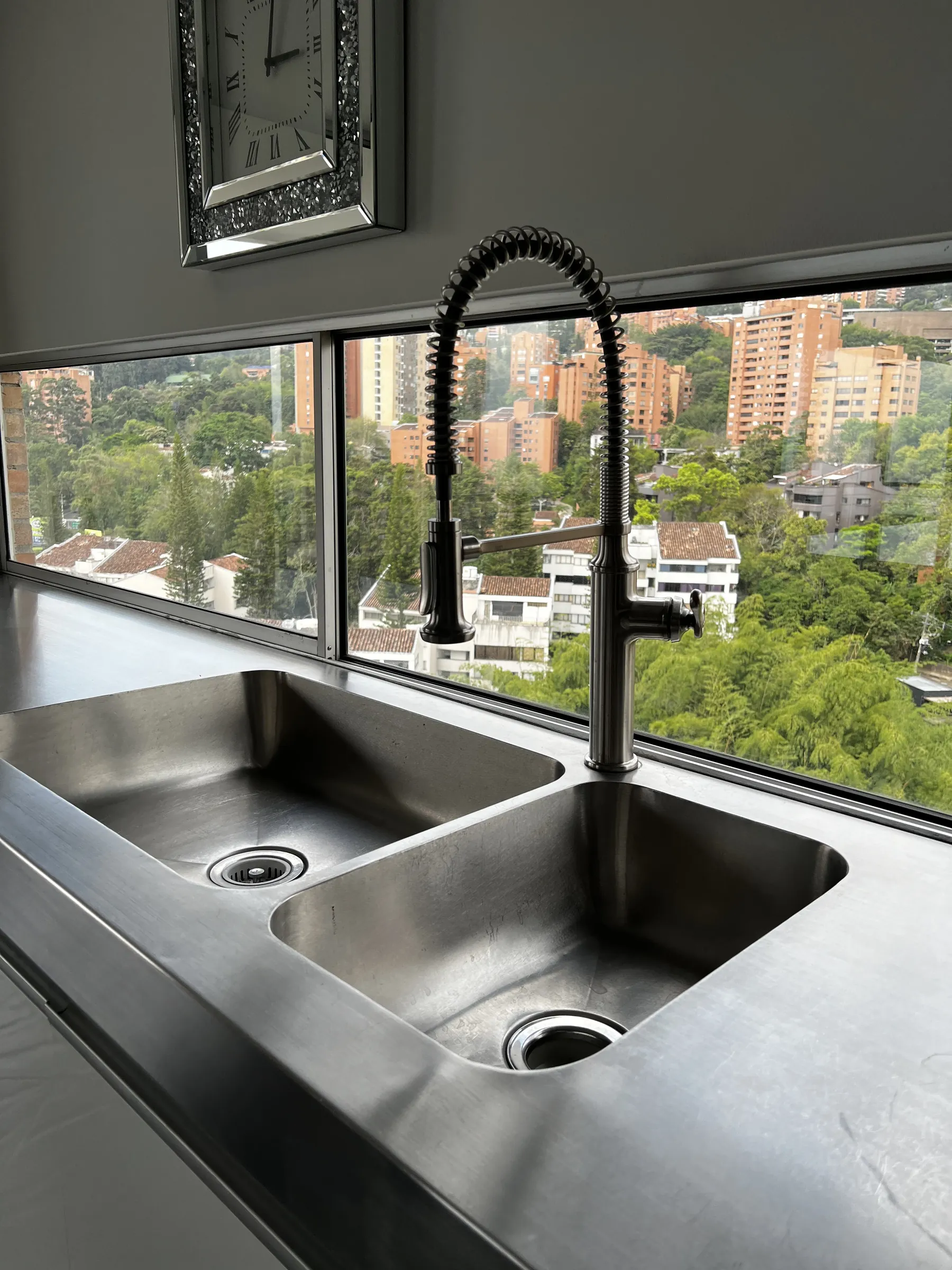 Stainless double sink and pull-down tap set into the counter beneath a window framing the green hillside